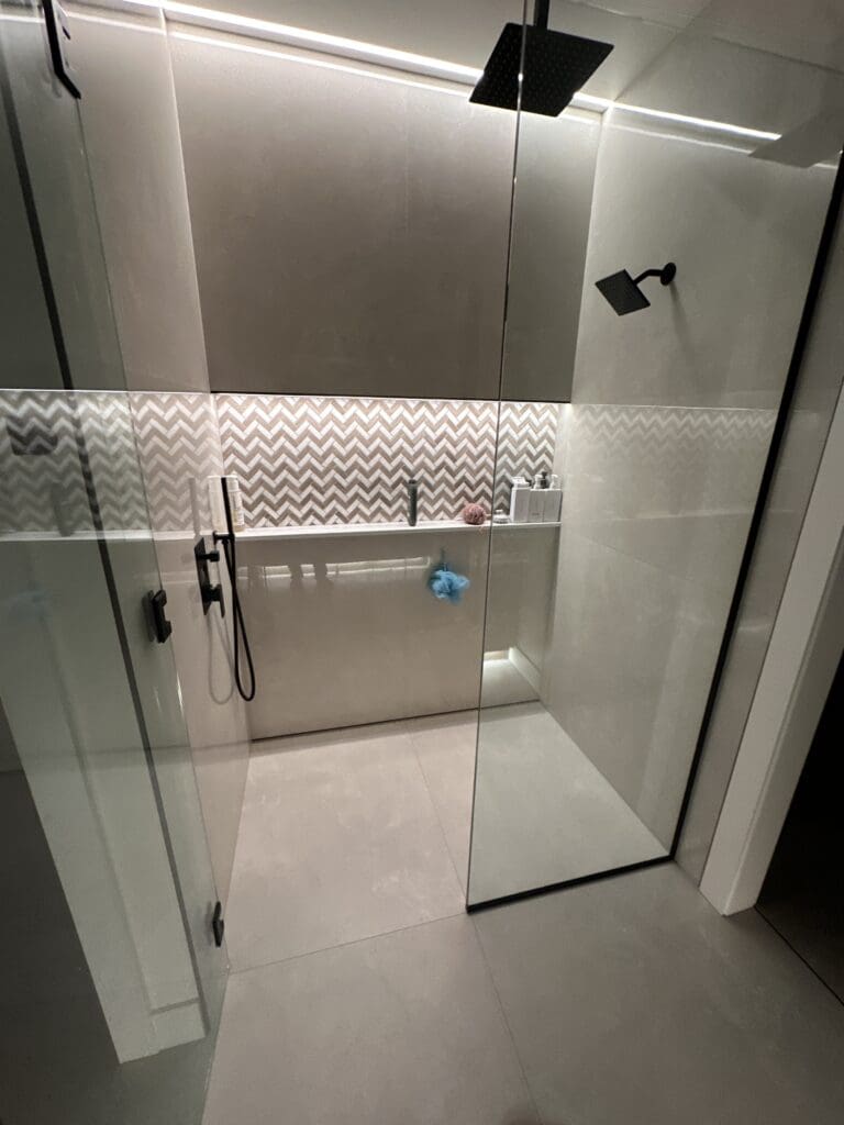 Frameless glass walk-in shower with large-format gray wall tile, chevron mosaic accent band, and matte black fixtures.