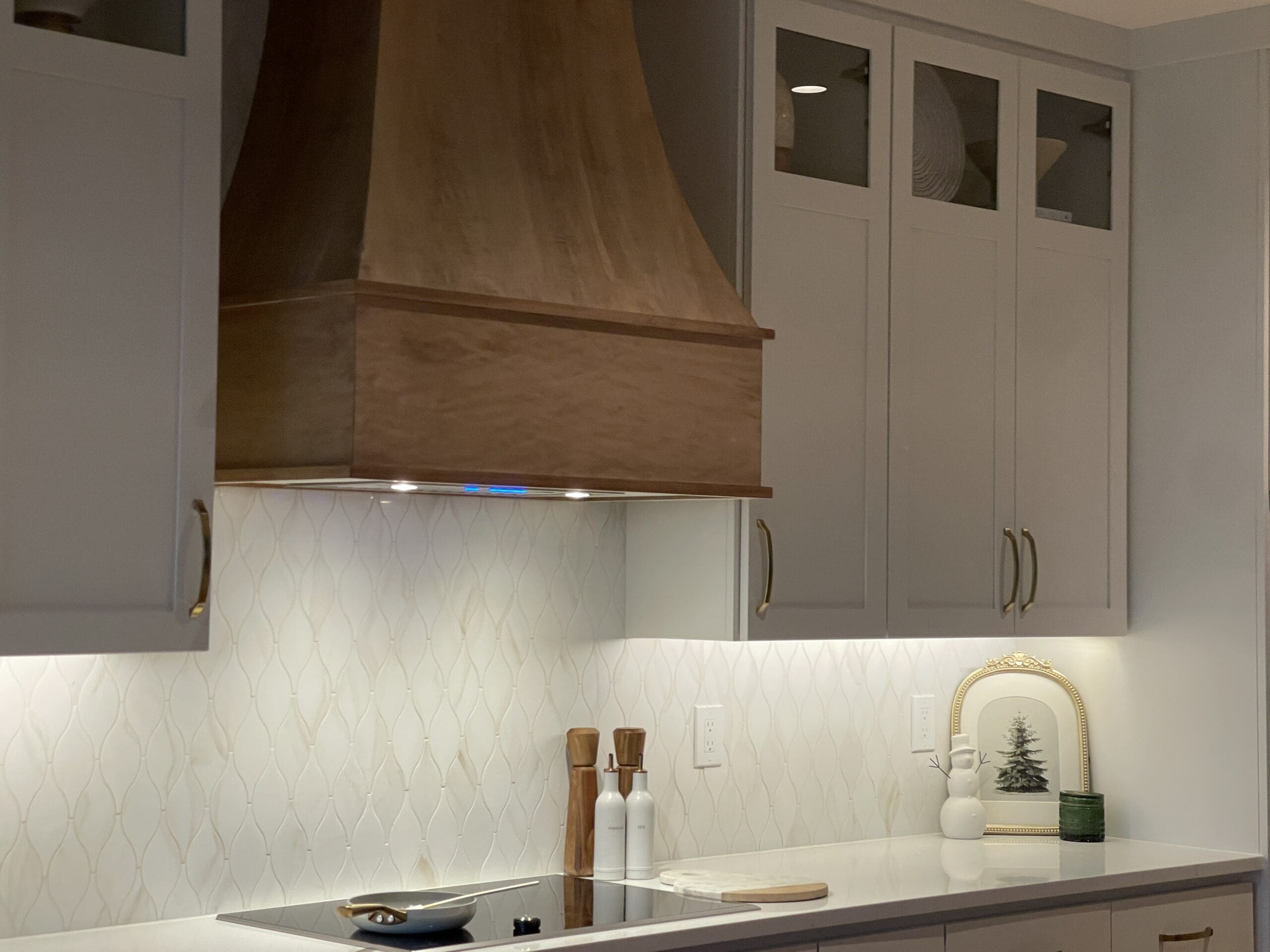 Modern kitchen with a custom wood range hood and white textured tile backsplash.
